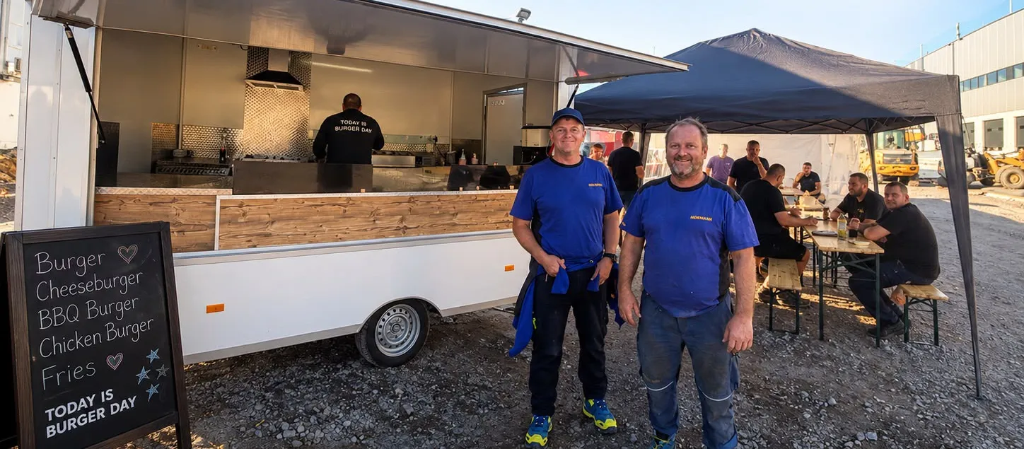 Burgerday-Cateringwagen bei einer Firmenfeier, Gäste an Bierzeltgarnituren